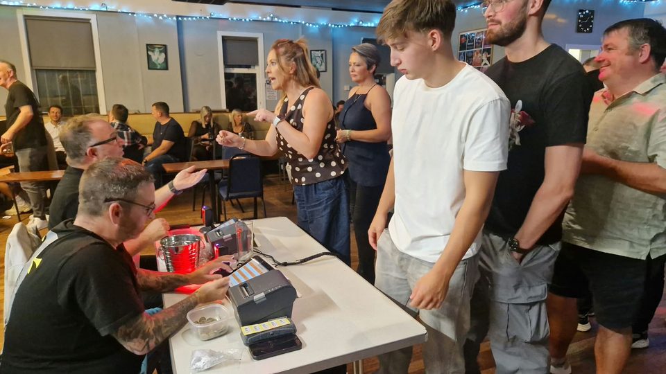 Guests queue at the race-night tote desk while helpers operate the ticket printers.