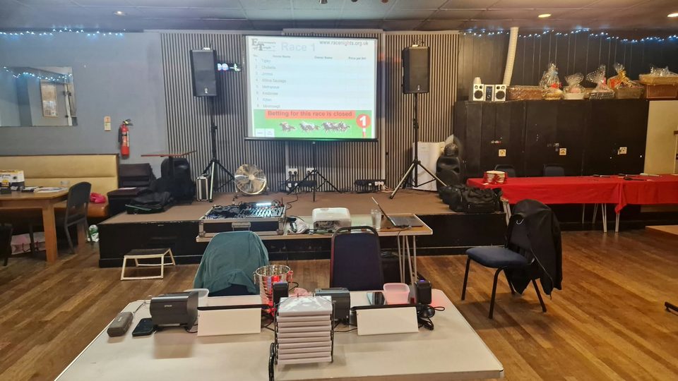 Race-night setup with projection screen, two PA speakers, sound mixer and tote desk.