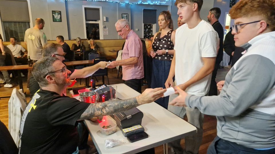 A helper hands a printed betting ticket to a guest at the tote desk.