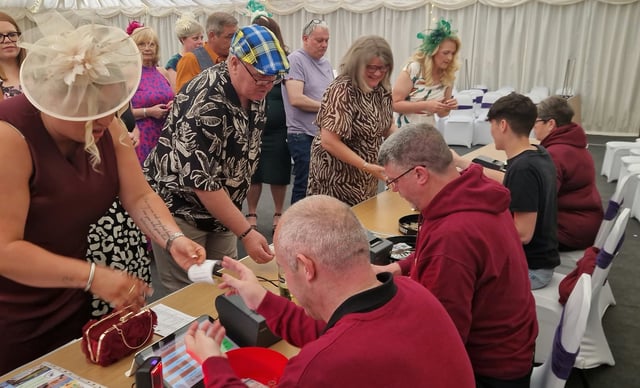 Guests and helpers exchanging printed betting tickets at the tote desk.