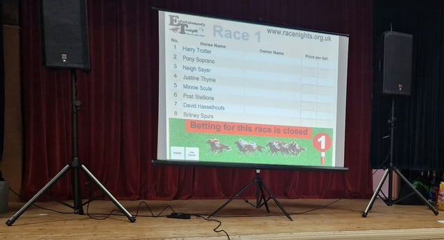 A branded race display on a projection screen with a PA speaker on either side.